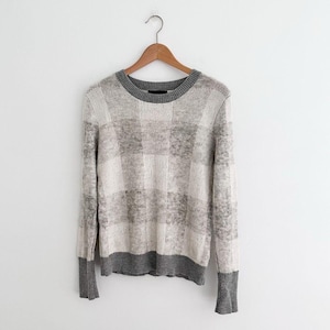 May include: A gray and white checkered sweater with a crew neck and long sleeves, hanging on a wooden hanger. The cuffs and neckline are a darker gray.