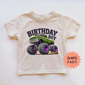 K&ouml;nnte beinhalten: Cremefarbenes T-Shirt mit einer Grafik eines gr&uuml;nen Monstertrucks mit lila Akzenten und dem Text "BIRTHDAY BOY" in Schwarz. Der Truck hat gro&szlig;e Reifen und ist auf einer Dirt-Track dargestellt.