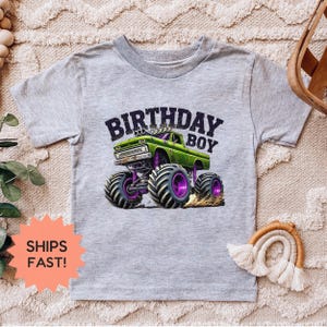 K&ouml;nnte beinhalten: Graues T-Shirt mit einem gr&uuml;nen Monster Truck-Design und dem Text "BIRTHDAY BOY". Der Truck hat lila R&auml;der und wirbelt Staub auf. Das Design ist mittig auf dem T-Shirt platziert.