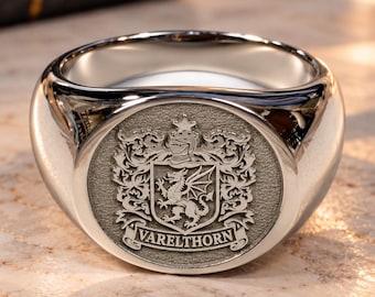 May include: A polished silver-toned signet ring featuring a circular face with an engraved heraldic crest. The design includes a dragon, a knight's helmet, and a star above a banner with the text VARELTHORN in capital letters.