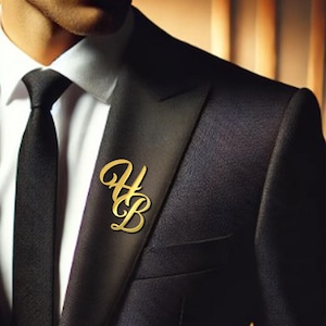 May include: A gold-colored lapel pin with the intertwined letters "HB" is affixed to a black suit jacket. The pin is in a cursive font and is positioned on the left lapel, near the chest. The jacket is paired with a black tie and a white dress shirt.