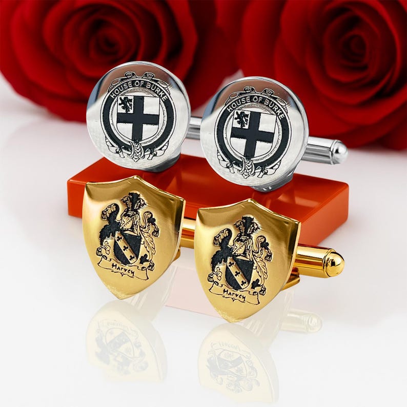 K&ouml;nnte beinhalten: Zwei Manschettenkn&ouml;pfe-Paare. Das obere Paar ist silberfarben mit einem schwarz-wei&szlig;en Emblem mit der Aufschrift "HOUSE OF BURKE" und einem schwarzen Kreuz. Das untere Paar ist goldfarben, schildf&ouml;rmig, mit Familienwappen und dem Namen "Harvey".