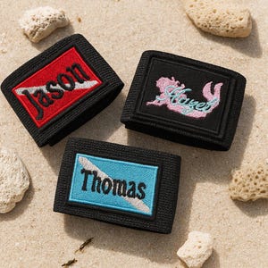 May include: Three black elastic bands featuring rectangular embroidered patches. One patch has a red background with the name Jason, one has a black background with a pink mermaid silhouette and the name Hazel, and one has a blue background with the name Thomas.