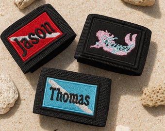 May include: Three black elastic bands featuring rectangular embroidered patches. One patch has a red background with the name Jason, one has a black background with a pink mermaid silhouette and the name Hazel, and one has a blue background with the name Thomas.