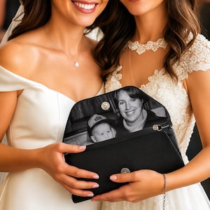 May include: A black clutch bag featuring a custom black and white photograph printed on the interior flap. The bag has a structured envelope shape with a metallic magnetic snap closure and a thin silver chain strap attached to the side.