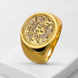 May include: A gold signet ring featuring an oval face with an embossed heraldic crest. The design includes two lions flanking a central shield with three symbols, topped by a crown. The text FAMILY is on the left and KENNEDY is on the right.