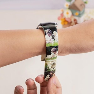 Puede incluir: Una correa de reloj personalizada con un diseño impreso que presenta fotos de niños y perros. La correa está sujeta a una caja de reloj plateada y se lleva en la muñeca. La correa es de color beige claro.