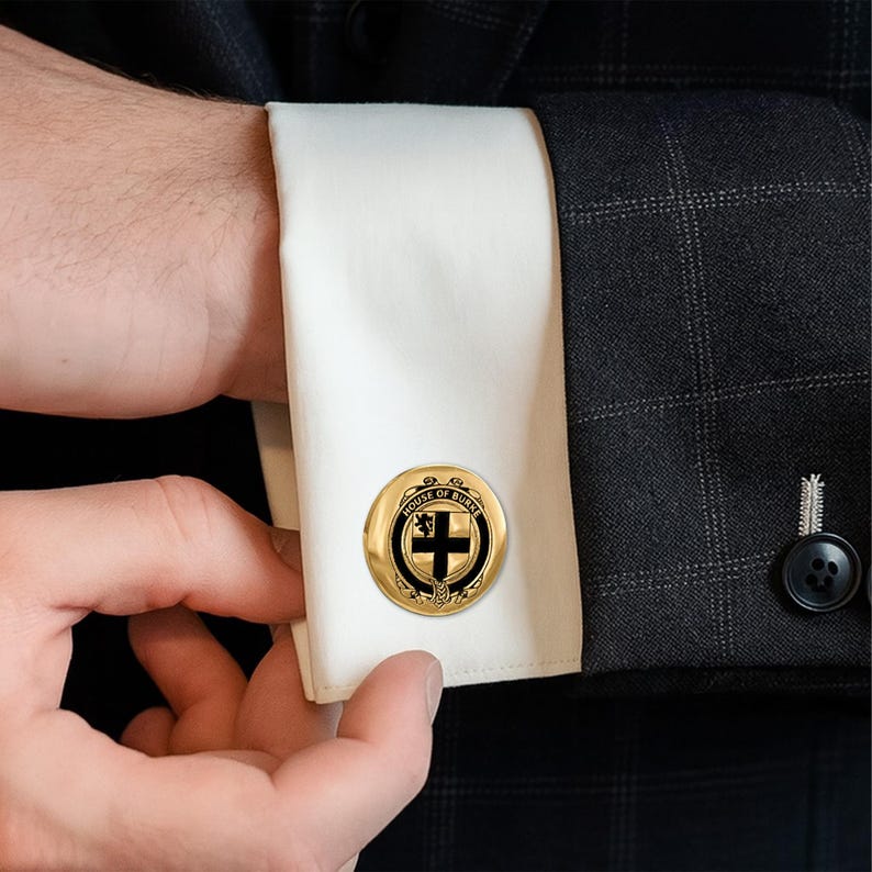 K&ouml;nnte beinhalten: Goldfarbene Manschettenkn&ouml;pfe mit einem schwarz-wei&szlig;en Emblem. Die runden Manschettenkn&ouml;pfe tragen den Text "HOUSE OF BURKE". Das Emblem enth&auml;lt ein Kreuz und einen L&ouml;wen. Die Manschettenkn&ouml;pfe befinden sich an einem wei&szlig;en Hemd&auml;rmel.