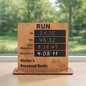 May include: Wooden running personal bests sign with the word "RUN" at the top. The sign displays times for 5k, 10k, half marathon, and marathon distances. The sign also includes the text "Vickie's Personal Bests" and a motivational quote.
