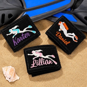 May include: Three black rectangular fabric patches featuring embroidered scuba diver figures and personalized names. One patch displays the name Karter in purple, one shows Daniel in orange, and one features Lillian in pink, all with white divers.