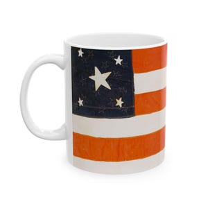 Può includere: Tazza in ceramica bianca con un design vintage della bandiera americana. Il design della bandiera include un campo blu con stelle bianche e strisce rosse e bianche. La tazza ha un manico curvo e una finitura lucida.