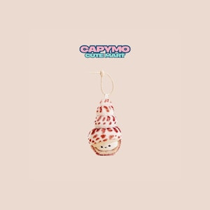 Peut inclure: Un ornement de coquillage fait à la main avec un visage souriant. La coquille est blanche avec des taches rouges et empilée en spirale. Il est suspendu à une ficelle beige. Le texte "CAPYMO CUTE MART" est au-dessus de l'ornement.