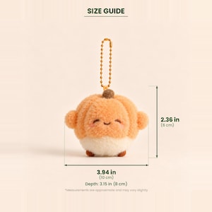 Puede incluir: Un llavero de calabaza de peluche con una cadena de bolas dorada. La calabaza tiene una parte superior naranja claro, una base blanca, un peque&ntilde;o tallo marr&oacute;n y una cara sonriente con mejillas rosadas. Mide 6 cm de alto, 10 cm de ancho y 8 cm de profundidad.