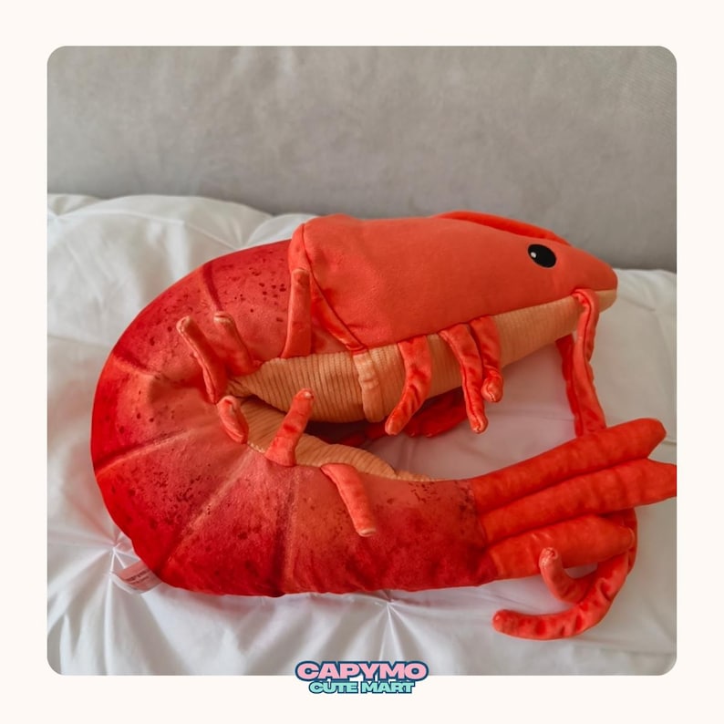 Puede incluir: Un peluche de langosta en tonos rojos y naranjas, con pinzas, patas y antenas detalladas. El juguete tiene una superficie suave y texturizada y un dise&ntilde;o lindo y de dibujos animados. La imagen incluye el texto "CAPYMO CUTE MART".
