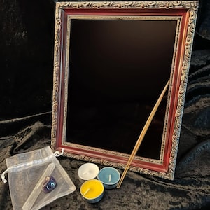 May include: A dark wood framed mirror with ornate gold trim, a small purple crystal, a white stick, a small bag, and three tealight candles in white, blue, and yellow.