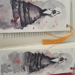 Puede incluir: Marcadores de acuarela con un diseño de ave estilizada y detalles en rojo, con borla. Los marcadores están colocados sobre un libro abierto, mostrando los detalles delicados y el estilo artístico.