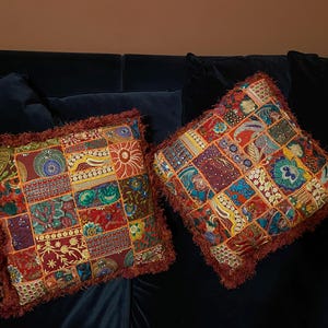 Puede incluir: Dos cojines de patchwork coloridos con bordes con flecos. Los cojines están hechos de diferentes telas y patrones en tonos de rojo, naranja, amarillo, verde, azul y marrón.