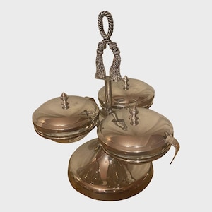 Peut inclure: Plat de service argenté à trois étages avec une poignée en forme de corde et trois couvercles. Chaque couvercle a un bouton sur le dessus.
