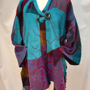 May include: A turquoise, purple, and brown patterned cardigan with a large green button. The cardigan has a V-neck and a fringed hem.
