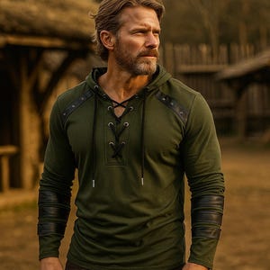 May include: Olive green hooded shirt with a lace-up neckline and black leather accents on the shoulders and sleeves. The long-sleeved shirt has a drawstring hood and is made of a soft, textured fabric.