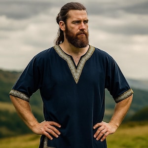 K&ouml;nnte beinhalten: Eine marineblaue Tunika mit goldenen Verzierungen am V-Ausschnitt und an den &Auml;rmeln. Das kurz&auml;rmelige Hemd hat ein dekoratives Muster und wird von einer Person getragen, die im Freien steht und die H&auml;nde in die H&uuml;ften gestemmt hat.