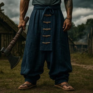 May include: Axe with a wooden handle and metal head. The person is wearing dark blue pants with decorative buttons and sandals. The background features a rustic village with wooden structures and a cloudy sky.