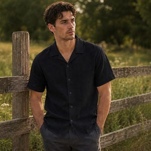 May include: A short-sleeved, dark navy blue button-down shirt featuring a classic camp collar neckline. The shirt is constructed with a straight hem and a central vertical row of matching dark buttons, providing a clean and structured appearance.
