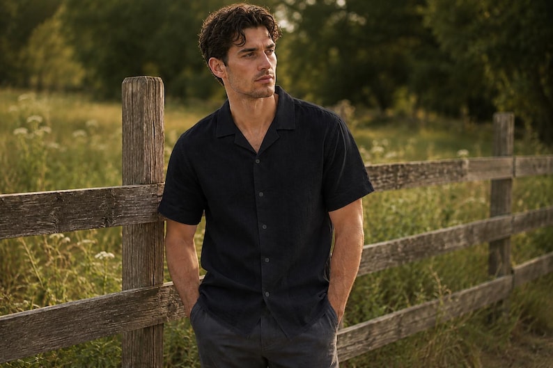 May include: A short-sleeved, dark navy blue button-down shirt featuring a classic camp collar neckline. The shirt is constructed with a straight hem and a central vertical row of matching dark buttons, providing a clean and structured appearance.