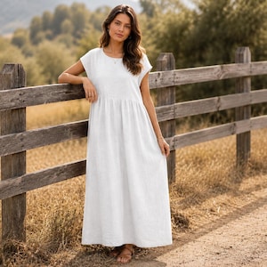 May include: A floor-length white maxi dress featuring short cap sleeves, a round neckline, and a gathered waistline that flows into a loose, full-length skirt. The garment is constructed from a solid, opaque fabric with a subtle, natural texture.