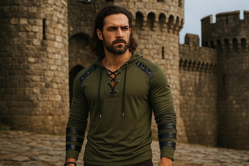 May include: An olive green hooded long-sleeve shirt with black leather accents on the shoulders and sleeves. The shirt features a lace-up neckline and is worn by a person standing in front of a stone castle.
