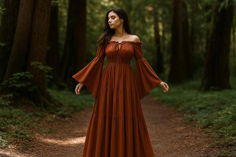 Puede incluir: Un vestido largo color &oacute;xido con hombros descubiertos y mangas largas acampanadas. El vestido presenta una falda escalonada y un detalle de lazo en el escote. La foto est&aacute; tomada al aire libre en un bosque.