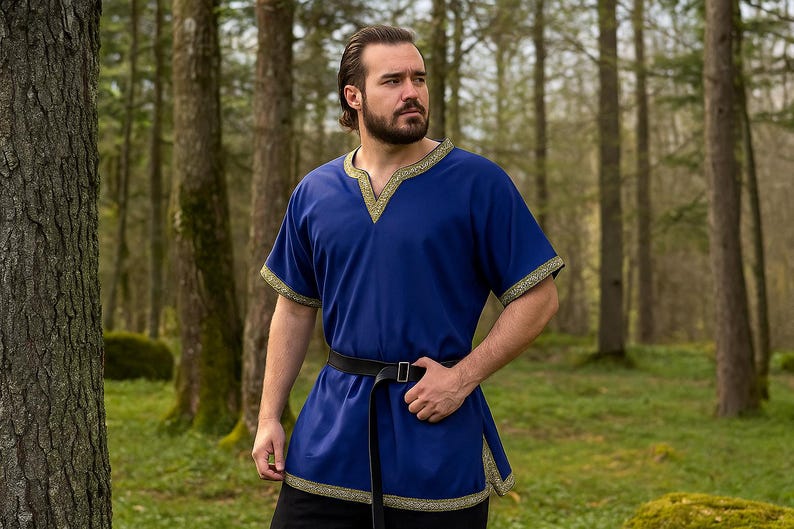 K&ouml;nnte beinhalten: Ein blaues Tunika mit goldenen Verzierungen am Ausschnitt und an den &Auml;rmeln sowie einem schwarzen G&uuml;rtel. Die Tunika hat einen V-Ausschnitt und kurze &Auml;rmel. Die Person steht in einem Wald.