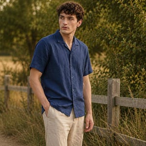 May include: A short-sleeved navy blue button-down shirt with a notched collar and a textured finish, paired with light beige trousers. The shirt features a straight hemline and a front button closure, providing a clean and simple look.