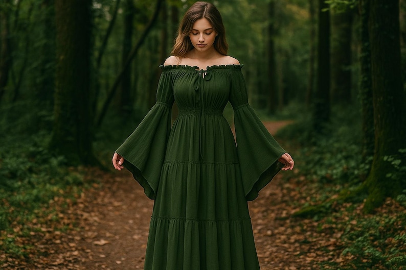 Puede incluir: Un vestido largo verde oscuro con hombros descubiertos, falda escalonada y mangas acampanadas. El vestido tiene un cuello con cord&oacute;n y se usa en un entorno forestal con un camino en el fondo. El vestido es de color s&oacute;lido.