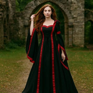 以下が含まれることがあります： 赤いトリムと長いフレアスリーブが付いた黒いドレス。 ドレスはハート型のネックラインと垂直の赤いストライプが特徴です。 女性は古い石のアーチの前で立っています。