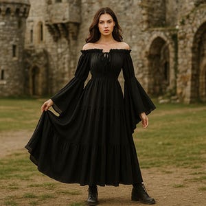 Puede incluir: Un vestido negro con hombros descubiertos, mangas largas y acampanadas y una falda escalonada. El vestido se lleva con botas negras. El fondo presenta un castillo de piedra y hierba verde.