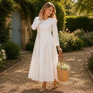 May include: A long-sleeved white midi dress featuring a V-neckline, a wrap-style bodice with side tie closures, and a full, flowing skirt. The dress is paired with a round, woven straw basket bag with brown leather handles filled with small white flowers.