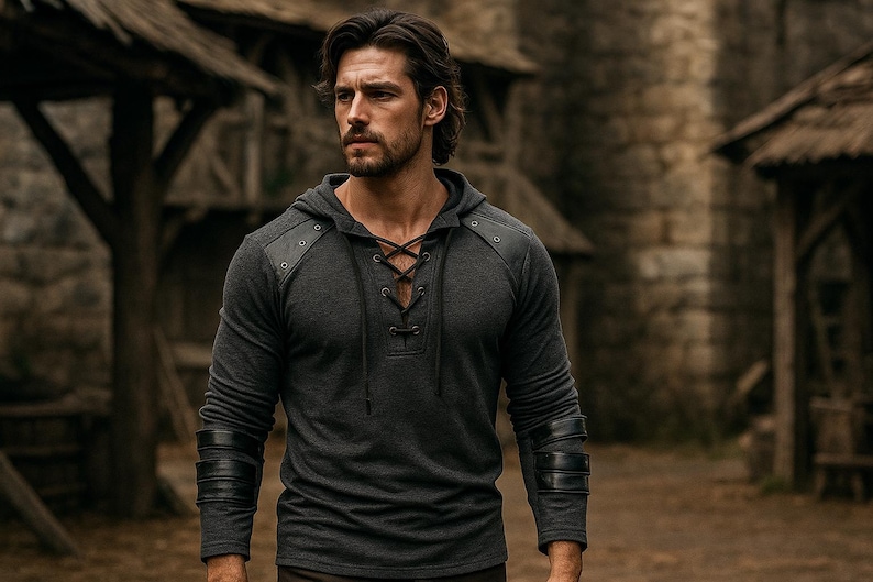 May include: A dark gray hooded shirt with leather accents on the shoulders and sleeves. The shirt features a lace-up neckline and is worn by a person in an outdoor setting. The sleeves have black leather bands.
