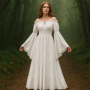 Puede incluir: Un vestido blanco con hombros descubiertos, mangas largas acampanadas y una falda escalonada. El vestido tiene un corpi&ntilde;o ajustado y un dise&ntilde;o largo y fluido. El fondo es un exuberante bosque verde con un camino.