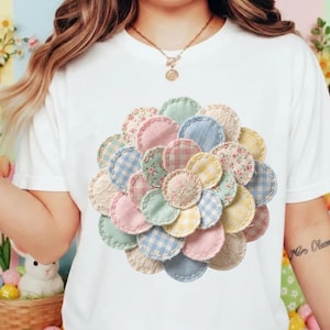 May include: White t-shirt featuring a large, circular design made of various pastel-colored fabric circles. The circles are in shades of pink, blue, yellow, and green, with floral and gingham patterns. The design is centered on the shirt.