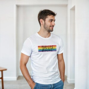 以下が含まれることがあります： 虹色の長方形のデザインが施された白いTシャツ。黒と赤の文字で「Straight & Co & ALLY」と書かれています。半袖のシャツは、青いジーンズを履いた人が着ています。