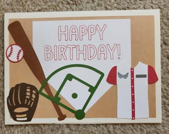 May include: A handmade birthday card with a baseball theme. The card features a baseball bat, ball, glove, and a baseball field graphic. The words "HAPPY BIRTHDAY!" are written in red.