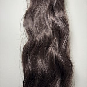 May include: A bundle of dark brown wavy human hair extensions.