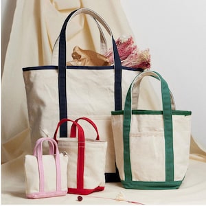 Peut inclure: Quatre sacs fourre-tout en toile de différentes tailles. Le plus grand sac est blanc avec une bordure bleu marine. Le deuxième plus grand sac est blanc avec une bordure verte. Les deux plus petits sacs sont blancs avec une bordure rouge et rose.