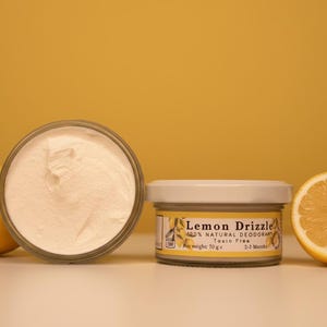Könnte beinhalten: Ein Glastiegel mit weißem Cremé-Deodorant, beschriftet mit Lemon Drizzle 100% Natural Deodorant Toxin Free net weight 70 g 2-3 Months, platziert zwischen einer ganzen gelben Zitrone und einer Zitronenhälfte vor gelbem Hintergrund.