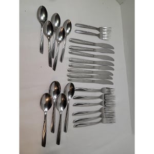 Pode incluir: Um conjunto de talheres de aço inoxidável, incluindo colheres, garfos e facas. As colheres têm uma tigela em forma de gota e uma alça canelada. Os garfos têm quatro dentes e as facas têm uma borda serrilhada. O conjunto está disposto sobre uma superfície branca.