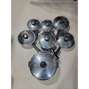 以下が含まれることがあります： ステンレス製の鍋とフライパンのセットで、お揃いの蓋が付いています。鍋には黒いハンドル、蓋には黒いノブが付いています。セットは明るい灰色の表面に配置されています。