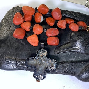 May include: A red gemstone necklace with a black cross pendant. The necklace is on a black wooden carving of a duck.