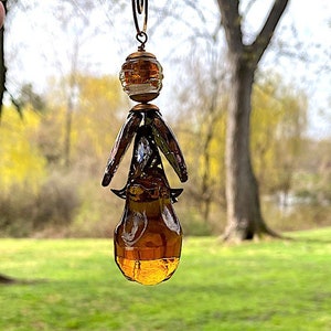 May include: A brown glass teardrop-shaped ornament with a copper wire design and a smaller round glass bead at the top.