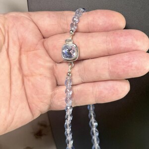 May include: A delicate necklace featuring a light blue, square-cut gemstone pendant set in a silver bezel. The necklace is strung with small, faceted, light blue beads. The design is elegant and suitable for special occasions.
